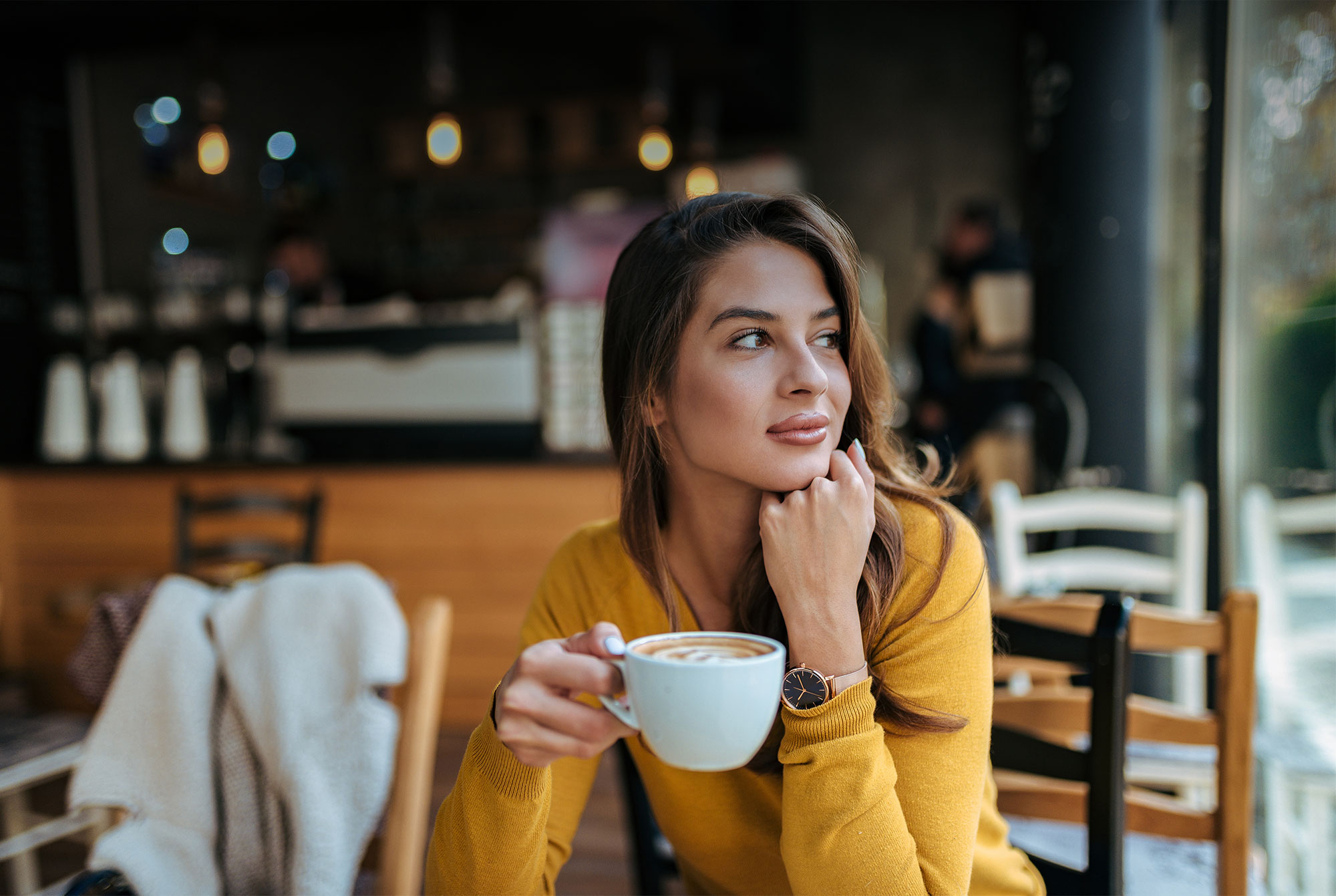 Woman sitting at coffee shop looking outside holding cup of coffee