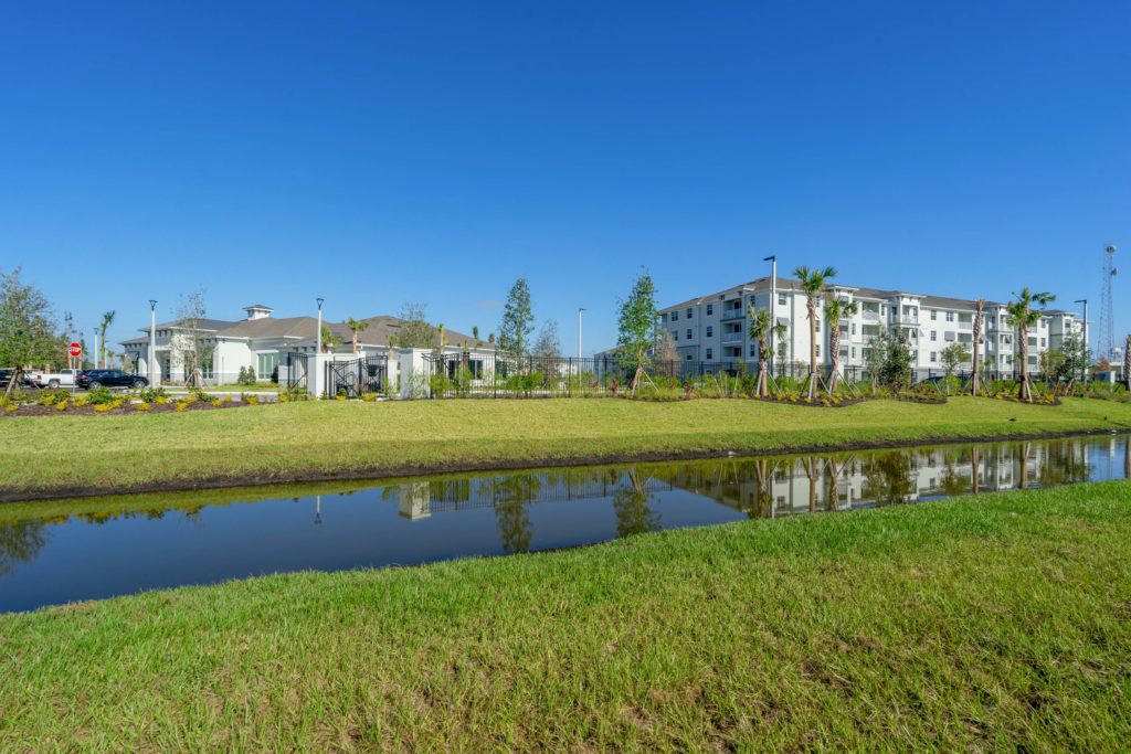 Apartment exterior with river, tropical landscaping, freshly cut yards, and blue sky